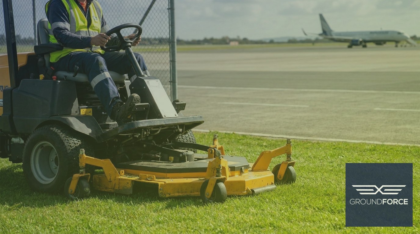 A grounds crew mowing the grass buffer zone along the perimeter of an airport runway.