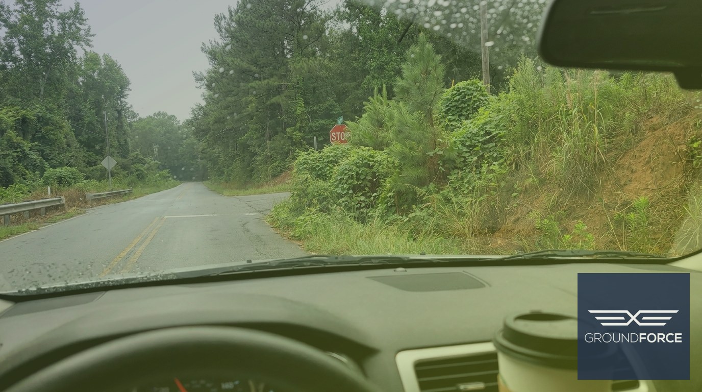 Overgrown roadside brush blocking driver sight distance at a Georgia highway intersection corner.